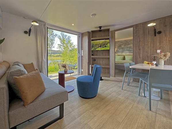 Un salon moderne comprenant un canapé, des fauteuils, une table à manger et une grande fenêtre donnant sur un paysage verdoyant.