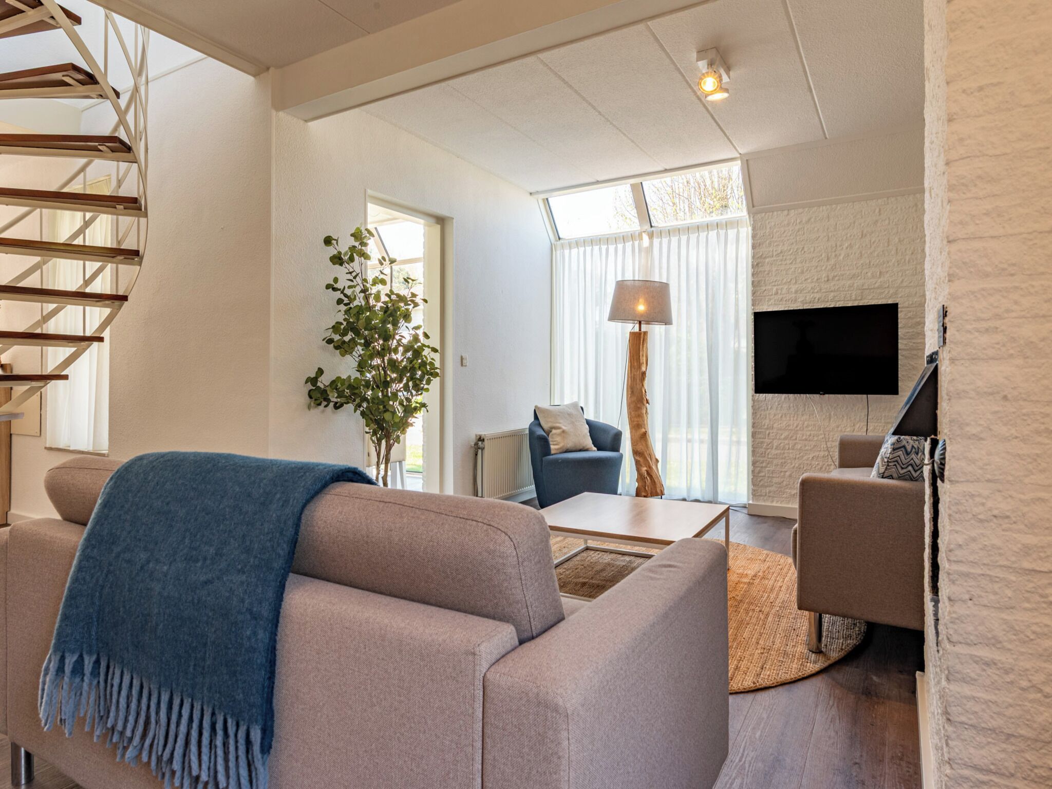 Un salon moderne avec un escalier, une grande fenêtre, un téléviseur à écran plat et une plante.