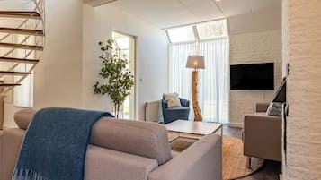 Un salon moderne avec un escalier, une grande fenêtre, un téléviseur à écran plat et une plante.