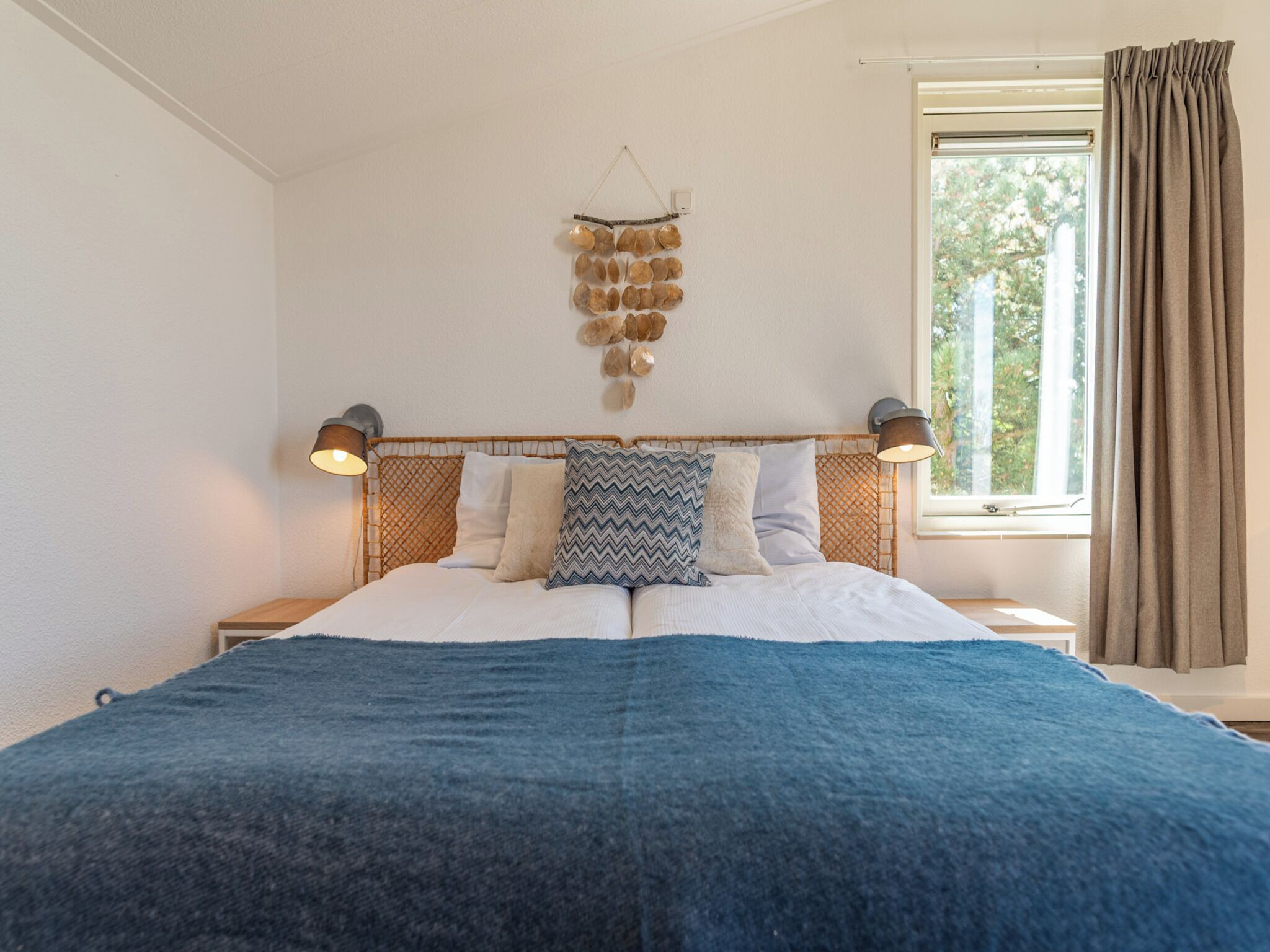 Een slaapkamer met een bed, twee bedlampen, een raam met gordijnen en een decoratie aan de muur.