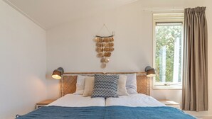 Una camera da letto con un letto, due abat-jour, una finestra con tende e un elemento decorativo al muro.