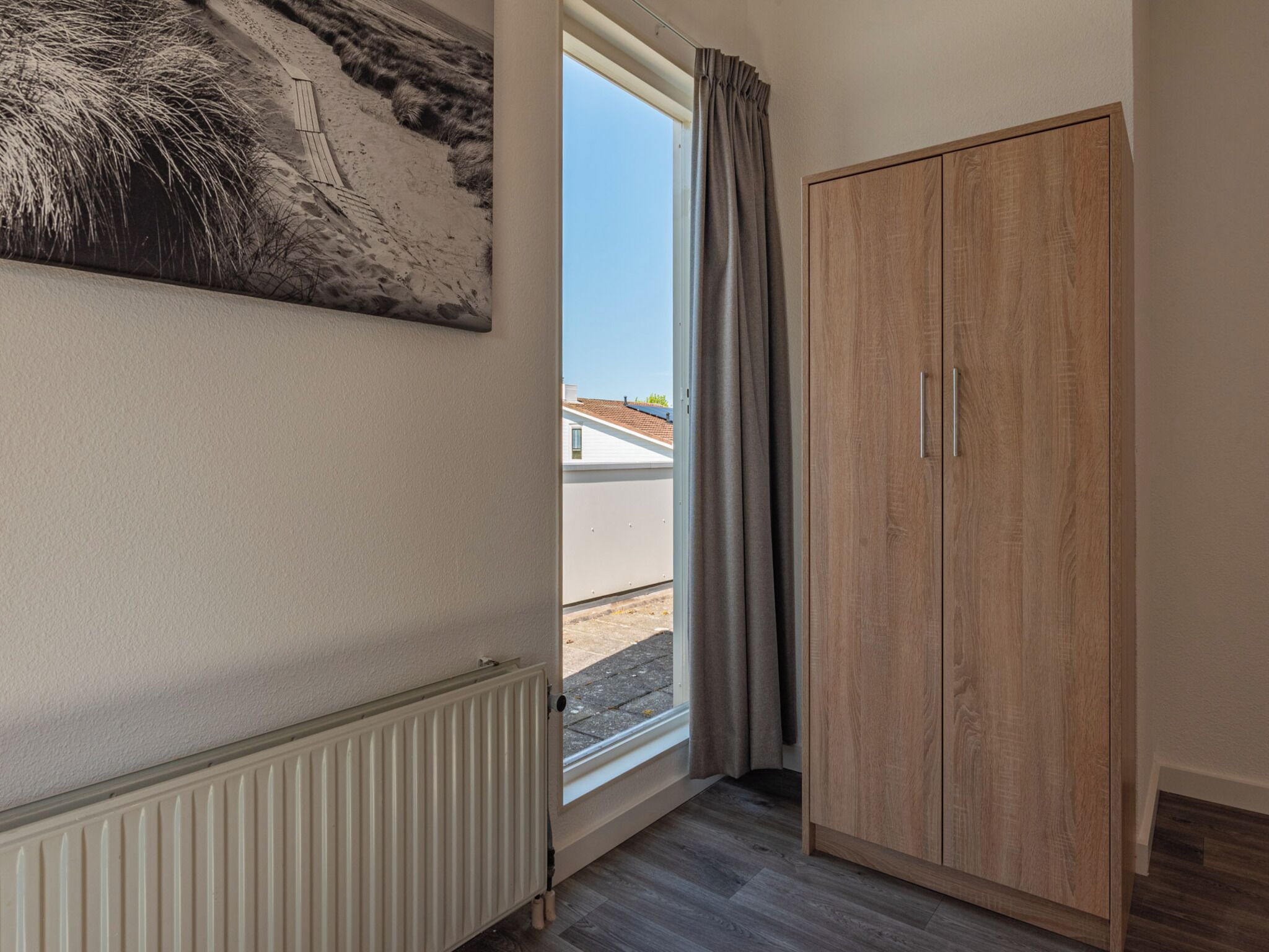 Habitació amb radiador, armari de fusta, finestra amb cortines i un quadre penjat a la paret.