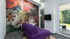 Ein modernes Wohnzimmer mit einem violetten Sofa, einem großen floralen Wandbild und einem Fernseher an der Wand.
