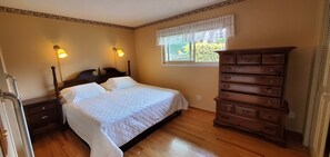 Un dormitorio con una cama, dos lámparas de noche, un tocador, una ventana con vistas y suelo de madera.