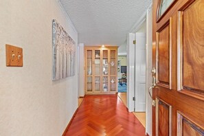 Een gang met houten vloer, een houten deur en een kast met glazen deuren.
