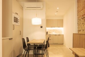 A modern kitchen with a wooden table and chairs, an air conditioning unit, and a hanging light fixture. - Guestready - Ariqus Apartments (L'Hospitalet de Llobregat)