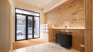 Eine Hotelhalle mit Backsteinwand, einer Rezeption, einem Garderobenschrank und einer Glastür zum Ausgang.