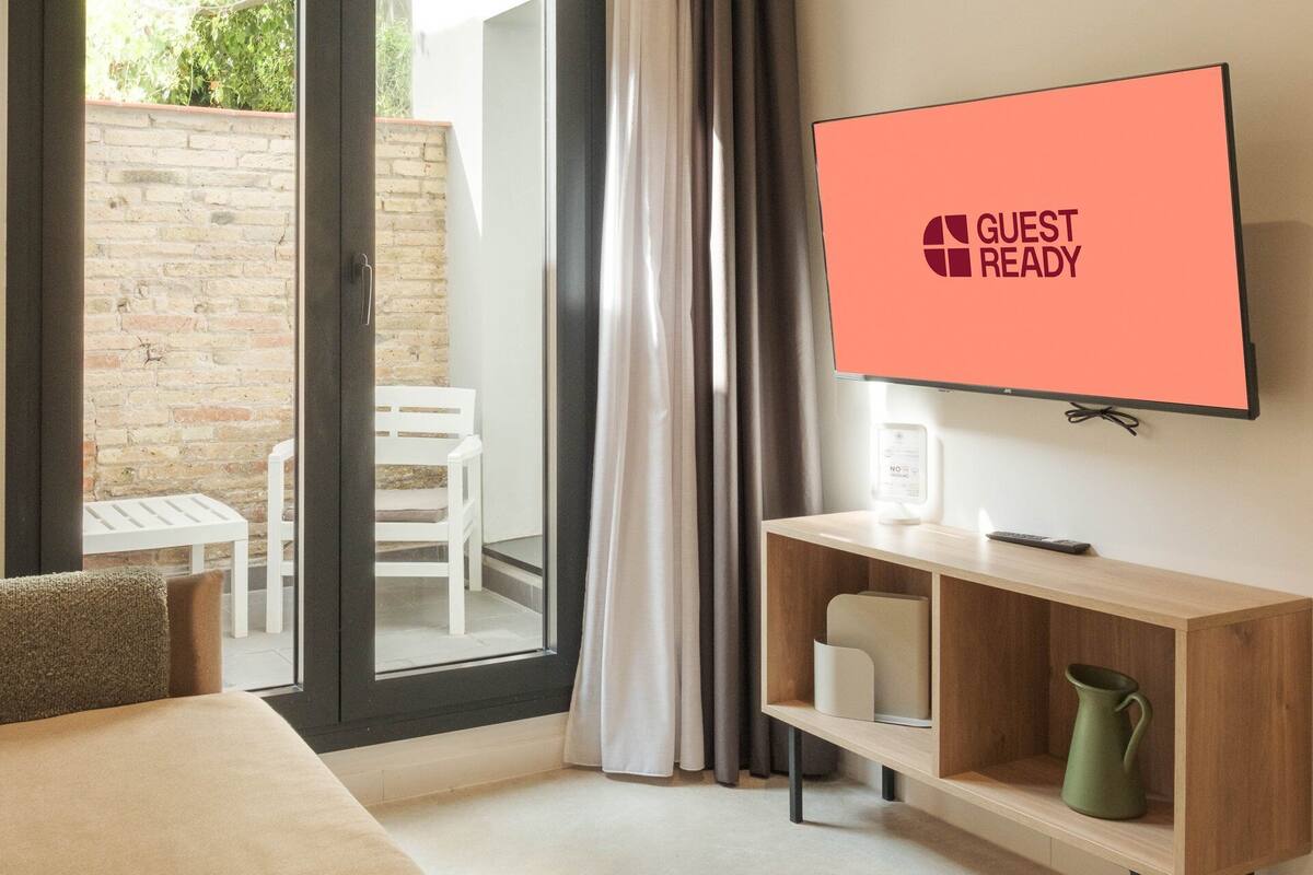 Ein Hotelzimmer mit Schiebetür zum Balkon, einem an der Wand befestigten Fernseher, einem kleinen Holzregal und einem Bett.