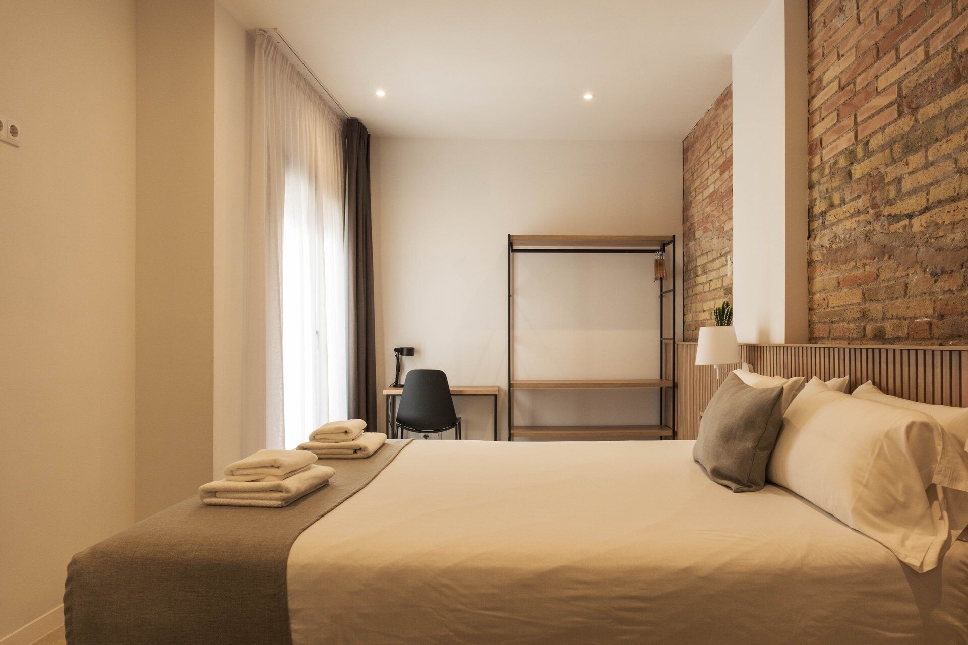 Ein Hotelzimmer mit Bett, Schreibtisch, Stuhl, Kleiderschrank und einer Ziegelwand.