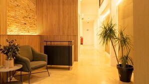 Eine moderne Lobby mit Backsteinwand, Holzvertäfelung, einer Couch, einem kleinen Tisch und einem Blumentopf.
