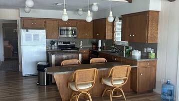 Une cuisine moderne avec des meubles en bois, un îlot central doté de chaises et des luminaires suspendus.
