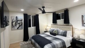 Ett modernt hotellrum med en säng, sängbord, en takfläkt och konstverk på väggarna.