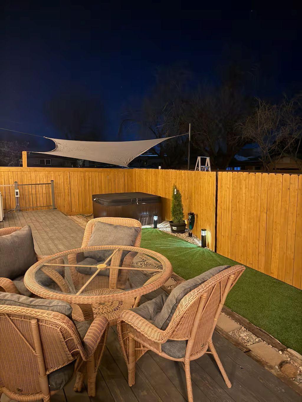 Een terras buiten met rieten meubels, een ronde tafel en een barbecue.
