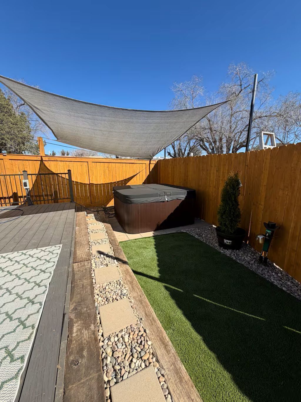 Een achtertuin met een houten terras, kunstgras, een jacuzzi en een houten omheining.