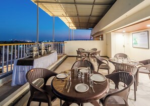 A rooftop terrace with tables set for dining, a view of the cityscape, and a signboard. - Treebo Vistara Gold Ujjain Junction (Ujjain)