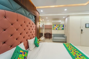 Una habitación de hotel con un cabecero capitonado, un escritorio, una silla, un sofá y una cama con un corredor estampado.