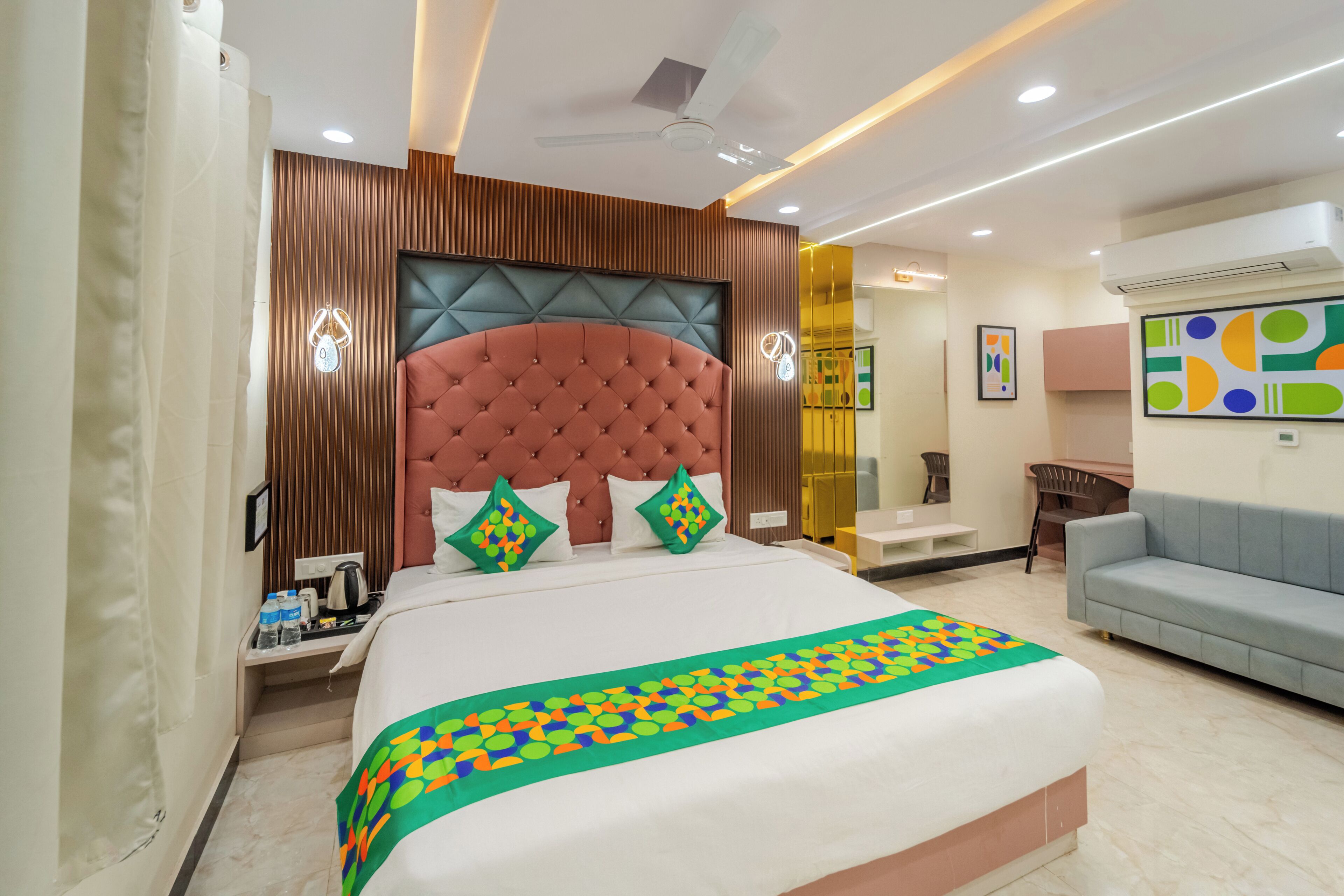 A modern hotel room with a large bed, a desk, a sofa, and a ceiling fan.