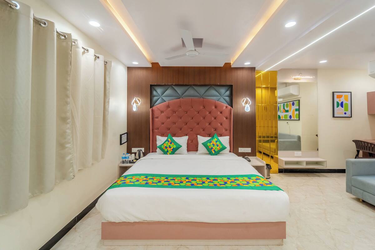 A hotel room with a large bed, a ceiling fan, recessed lighting, a wooden headboard, and a seating area with a sofa.