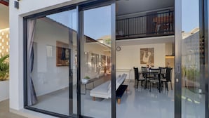 A modern interior with a glass door leading to a balcony, a dining area with a table and chairs, and a sofa. - Collection O near Sanur Beach formerly  (Denpasar)
