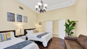 Hotelkamer met twee bedden, een kroonluchter, kunstwerken aan de wanden, een potplant en een leren bank.