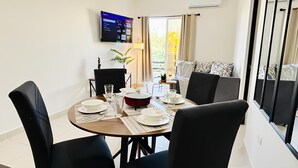 Uma área de refeições com uma mesa redonda, cadeiras pretas e uma televisão de tela plana na parede.