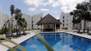 Piscina com espreguiçadeiras e um pavilhão com cobertura de palha.