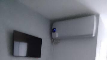 Une pièce avec un bureau en bois, une chaise rouge, un climatiseur fixé au mur et un lit recouvert d’une couvre-lit à motifs.
