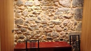 Zona pranzo con parete in pietra, tavolo e sedie in legno.