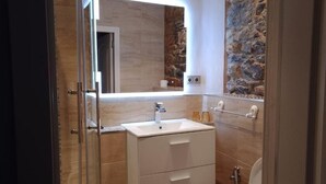Un bagno moderno con un mobile vanitario bianco, uno specchio e una parete in pietra.