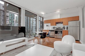 Une cuisine moderne avec des meubles en bois, un réfrigérateur en acier inoxydable et un coin repas comprenant une table et des chaises blanches.