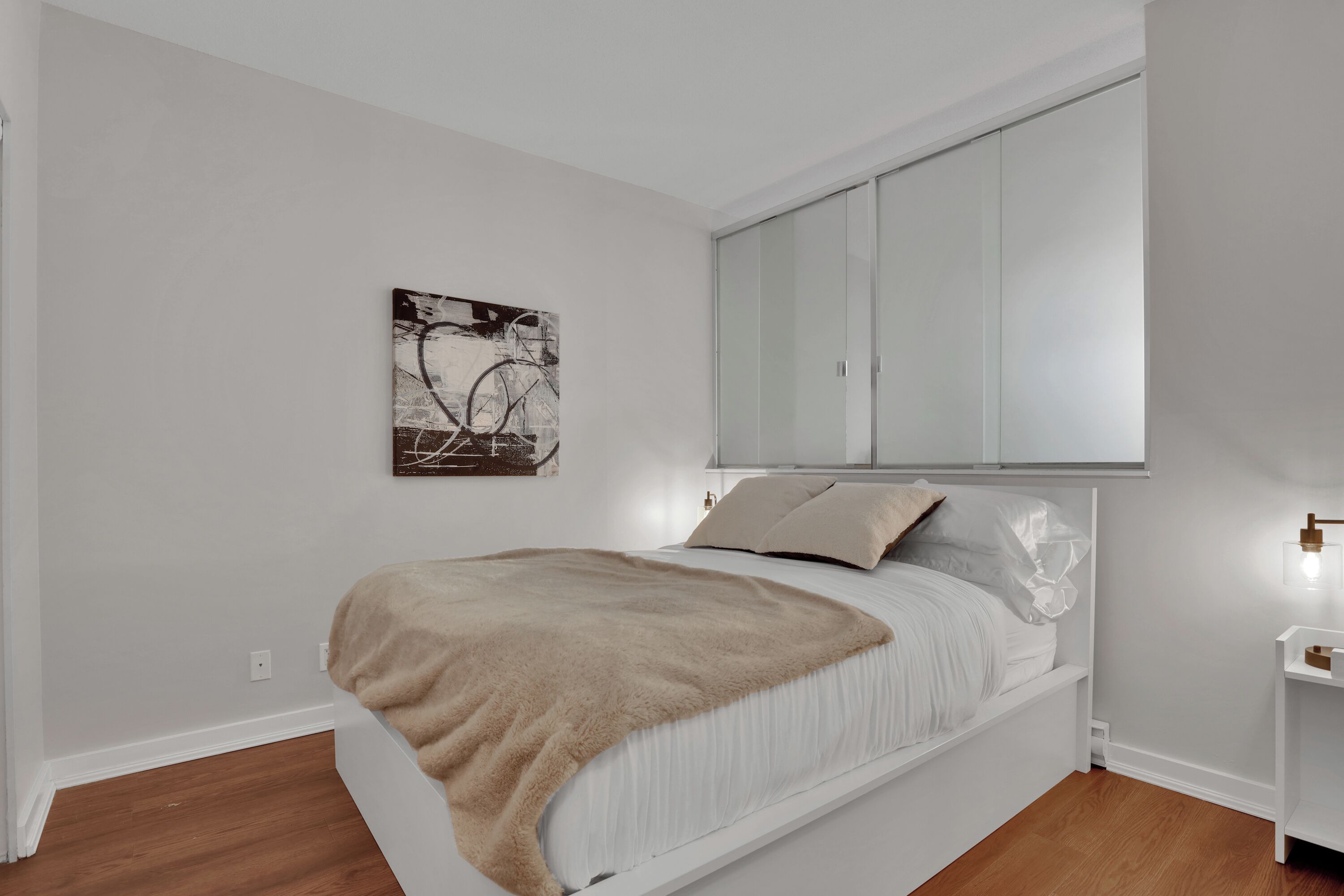 A bedroom with a bed, a bedside table, a mirror, and a wall-mounted artwork.