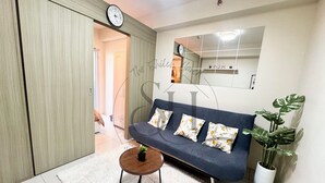 A living room with a sofa, a small round table with a plant, a white rug, a clock, and a mirror on the wall. - High Floor Manila Bay View, Near MOA & Airport (Pasay City)