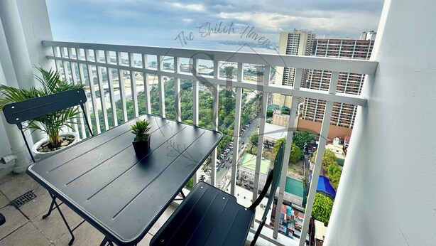 A balcony with a table and chairs, a potted plant, and a view of a cityscape. - High Floor Manila Bay View, Near MOA & Airport (Pasay City)