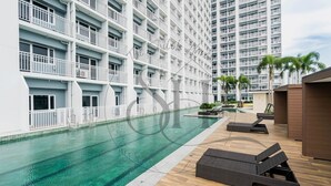 A swimming pool with lounge chairs and a high-rise building in the background. - High Floor Manila Bay View, Near MOA & Airport (Pasay City)