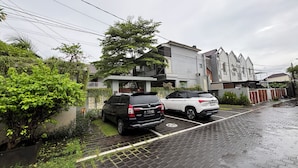A residential street with two parked cars, a gated house, and a building with a sloped roof. - Collection O near Sanur Beach formerly (Denpasar)
