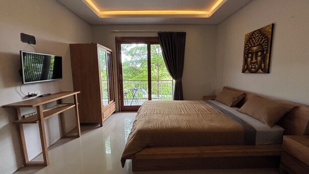 A bedroom with a bed, a TV, a desk, and a balcony with a view of greenery. - Collection O near Sanur Beach formerly (Denpasar)