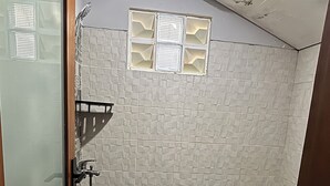 A bathroom with a shower, toilet, and a small window with a grid pattern. - Collection O near Sanur Beach formerly (Denpasar)