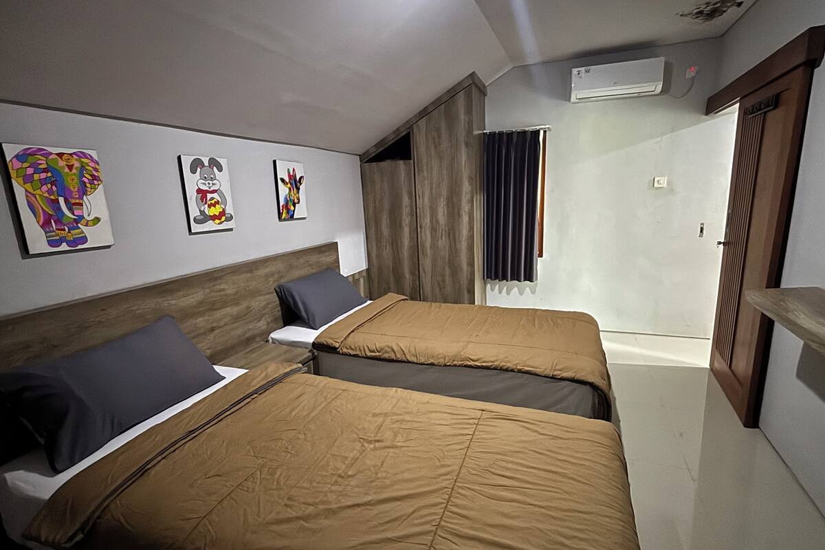 A hotel room with two beds, a wooden headboard, a wall-mounted air conditioner, and a door leading to another room.