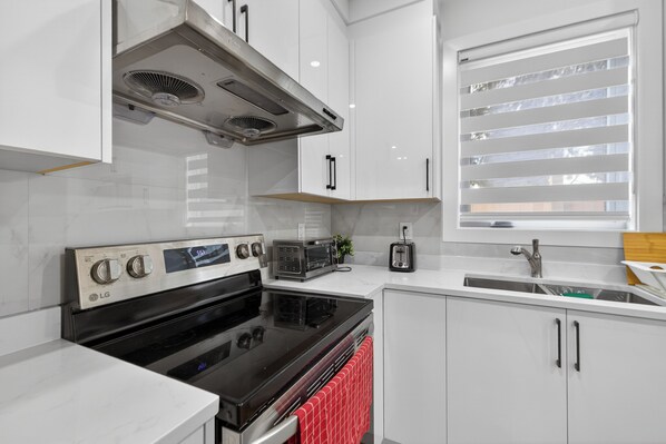 Eine moderne Küche mit weißen Schränken, einem schwarzen Herd, einem eingebauten Backofen, einer Mikrowelle, einem Toaster und einem Fenster mit Jalousien.