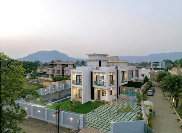 A modern two-story house with a flat roof, a spacious patio, and a view of the surrounding neighborhood. - The White Casa Villa (Devghar)