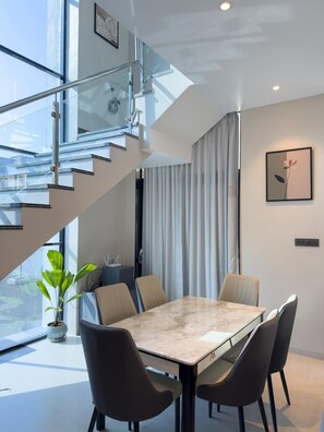 Un comedor moderno con una mesa de vidrio, cuatro sillas, una planta en maceta y una escalera con barandillas de vidrio.