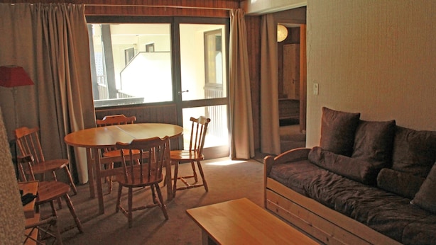 Uma sala de estar com uma mesa de jantar de madeira, cadeiras, um sofá e uma janela com cortinas.