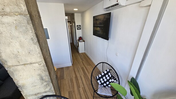 A modern interior with a wooden floor, a black chair with a polka dot pillow, a striped rug, and a large green plant. - Apartment Torremolinos Near Bajondillo Beach (Torremolinos)