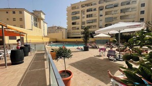 A rooftop pool area with lounge chairs, potted plants, and a building with multiple balconies in the background. - Apartment Torremolinos Near Bajondillo Beach (Torremolinos)