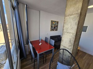 Ein kleiner, moderner Raum mit einem roten Tisch, schwarzen Stühlen, einem schwarzen Sofa und einem großen Fenster mit Vorhängen.