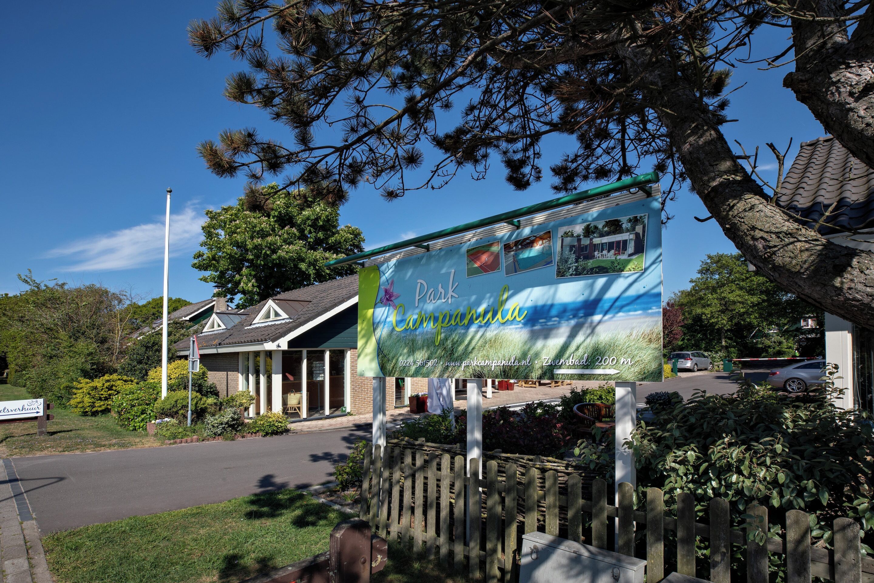 A sign for Park Campanula with a house and a wooden fence in the foreground.