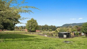 A rural landscape with a fenced field, a small building, and distant hills.