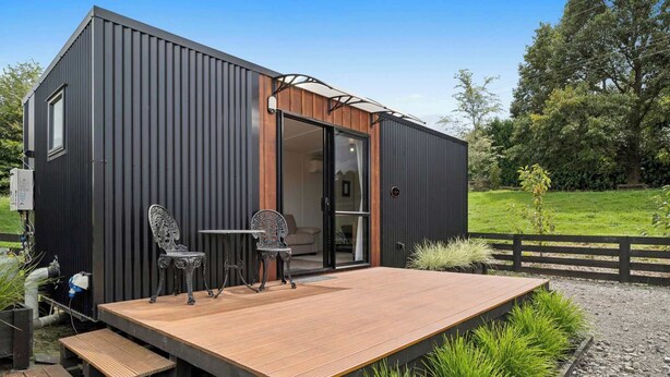 A modern, compact building with a wooden deck, metal chairs, and a table.