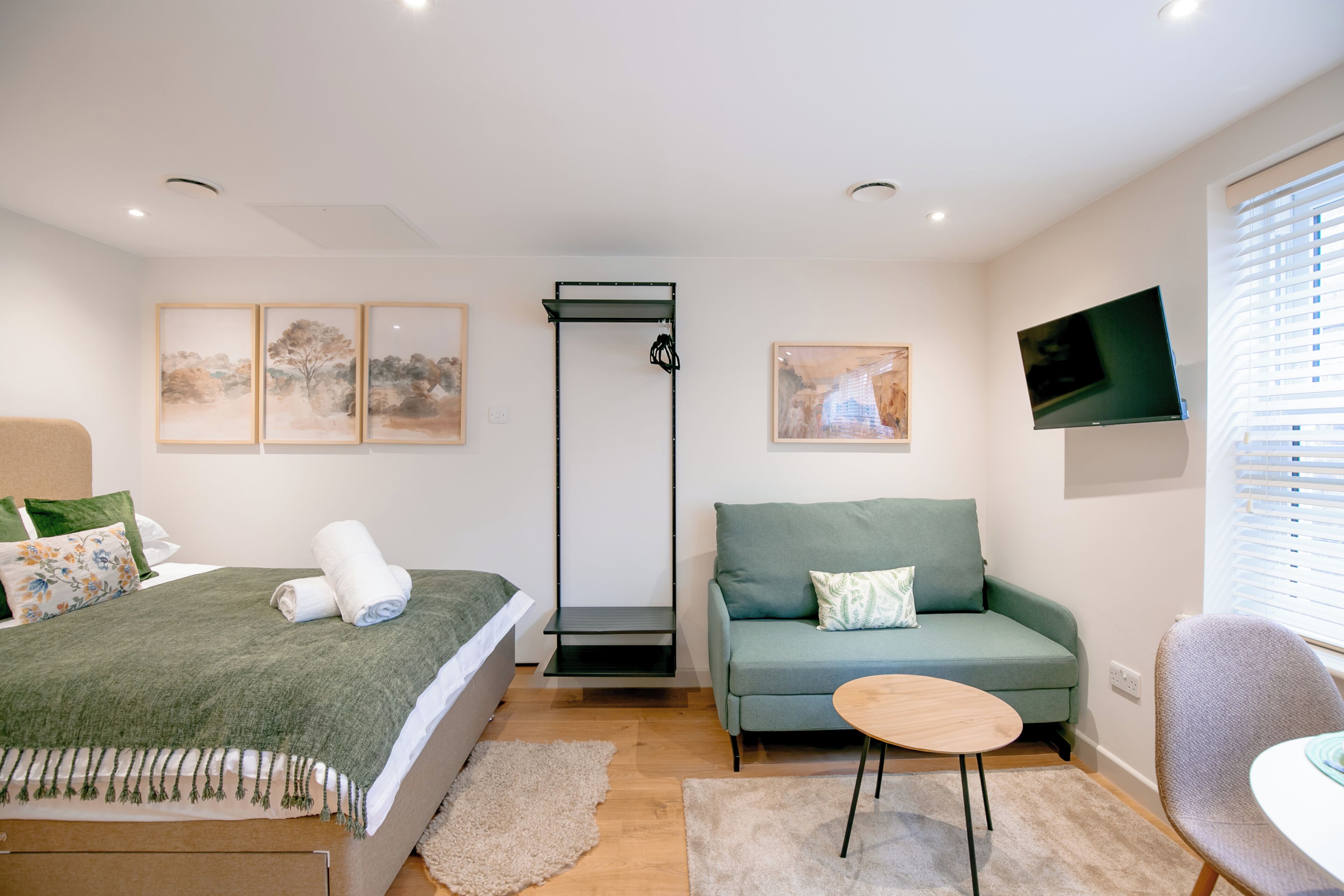 Un dormitorio moderno con cama, sofá, una mesita y televisor.