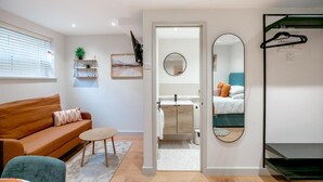 A modern room with a sofa, a small table, a mirror, and a bed with a green headboard.